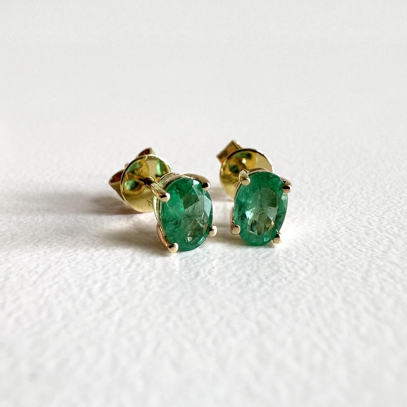 single tulip oval emerald earrings in 18k gold on table