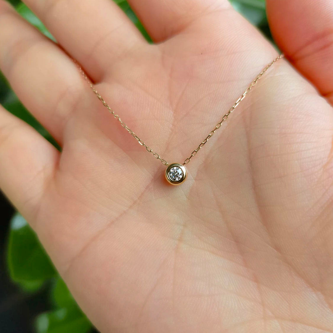 0.15ct diamond bezel necklace in 18k gold on hand