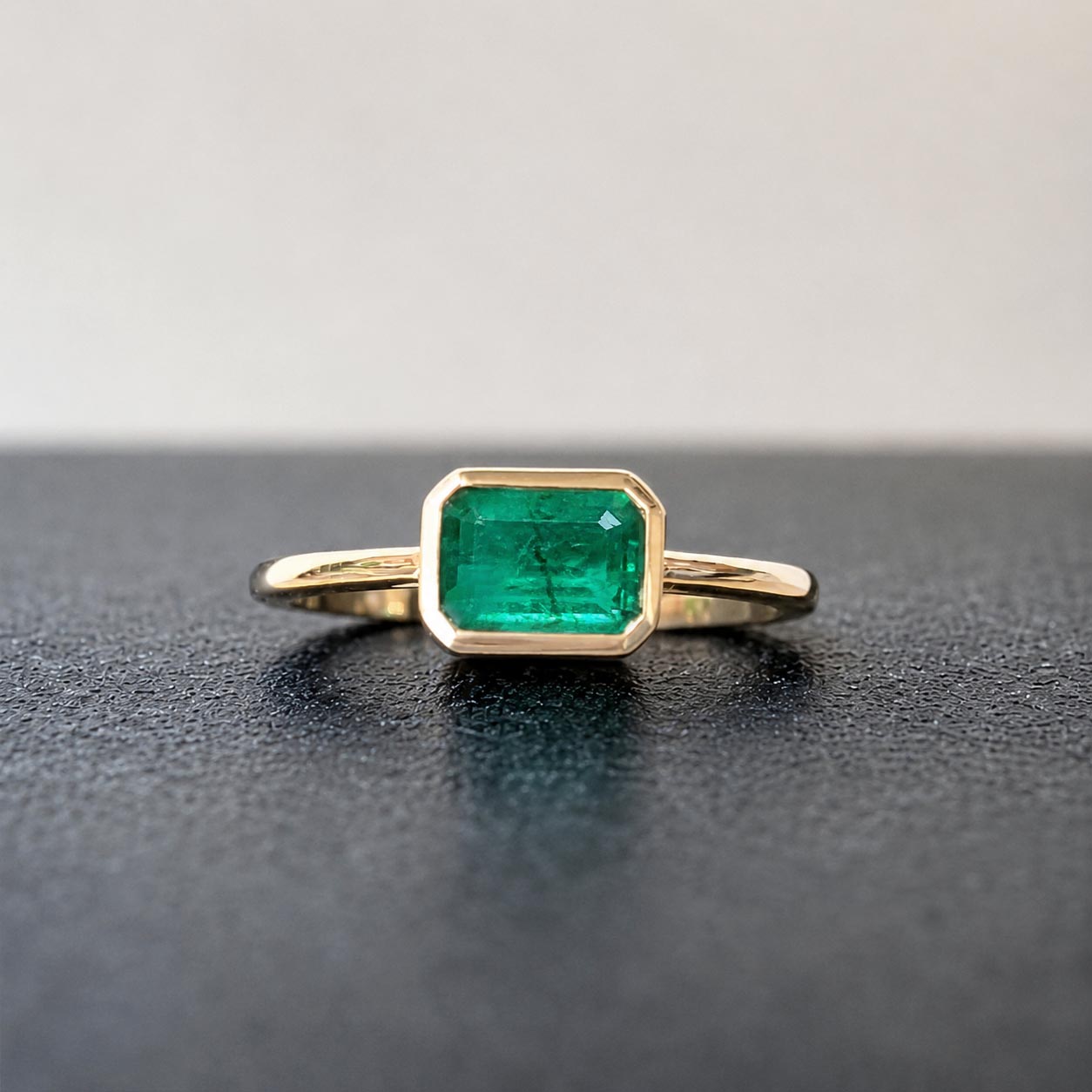 1.0ct step cut emerald ring in 18k gold on table