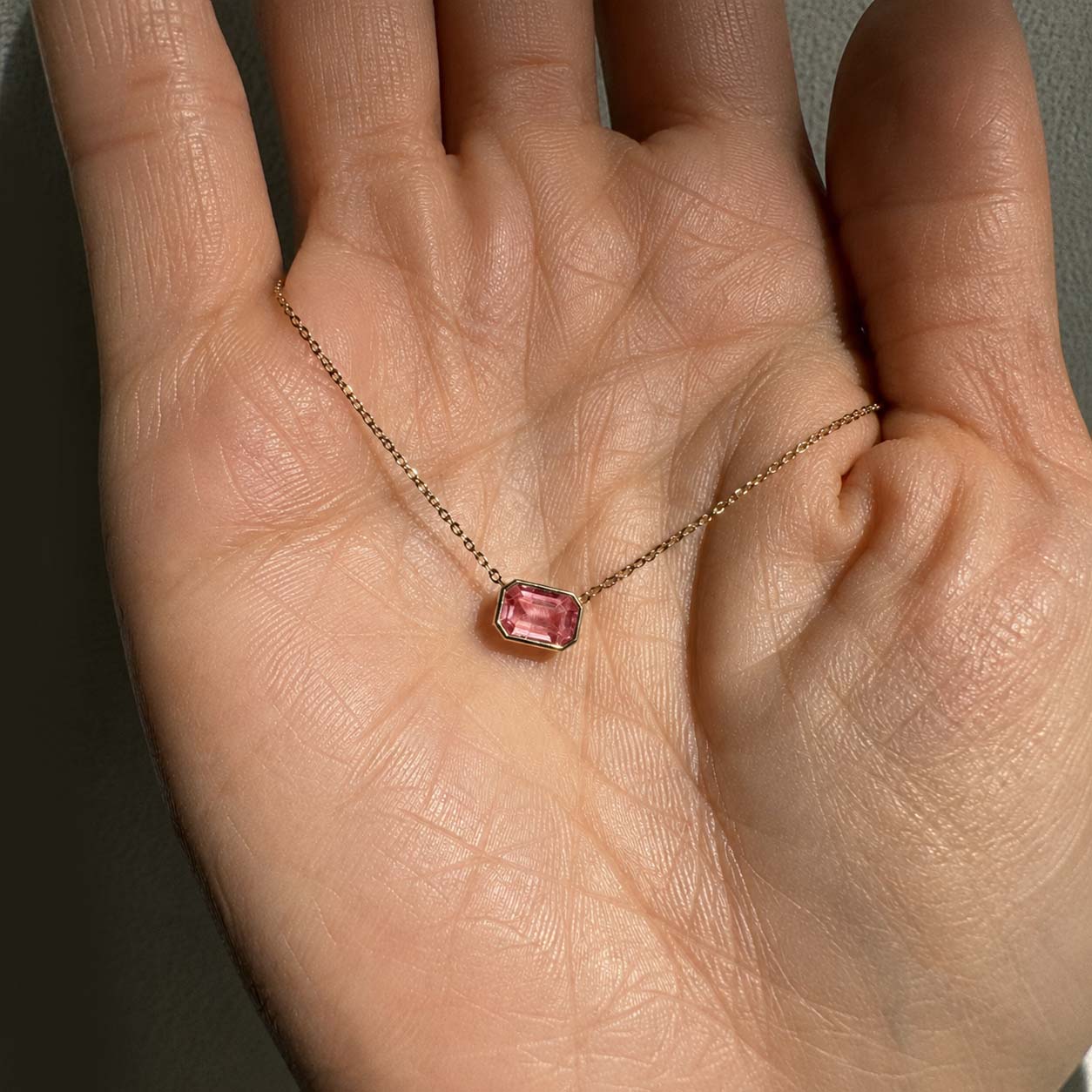 ooak bezel set padparadscha sapphire necklace in 18k gold on hand